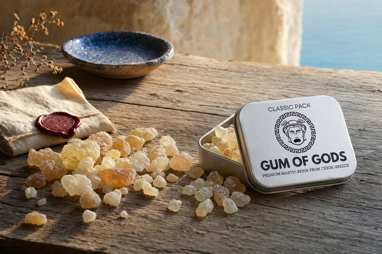 Open white mastic tin on rustic Mediterranean wood beside folded cream parchment with a deep red wax seal and a small Mediterranean blue ceramic dish in soft focus.