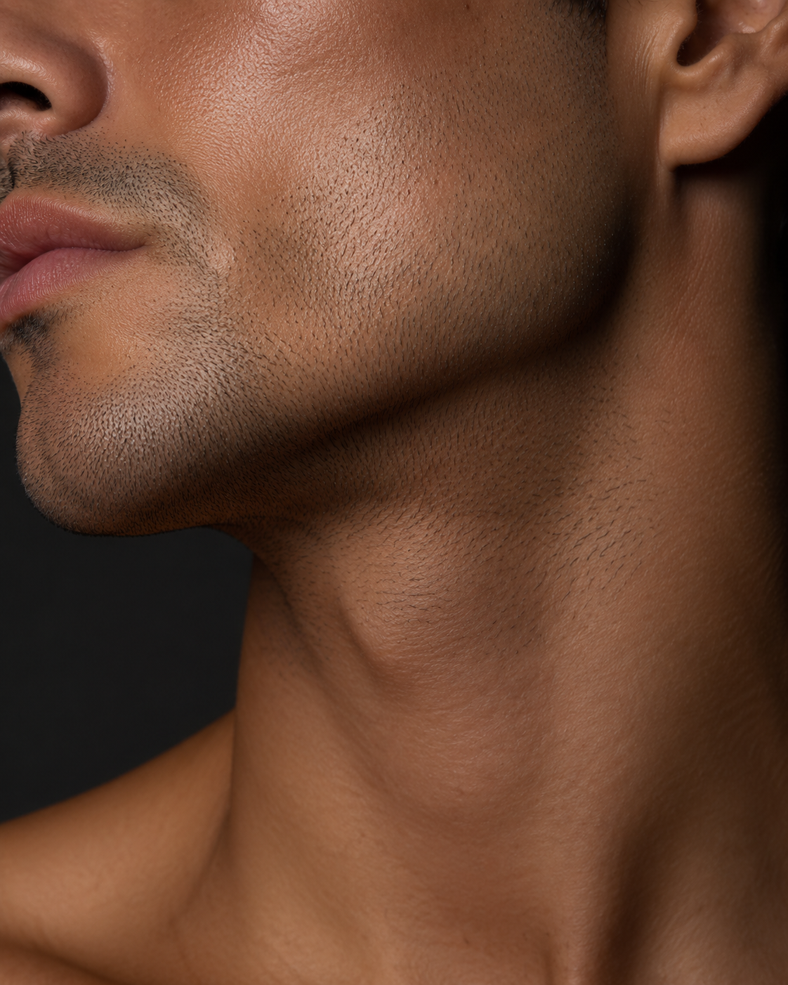 Defined male jawline and neck close up in warm studio light.